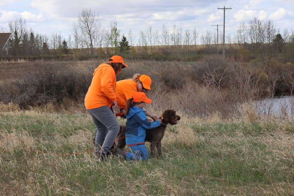 two women and a child standing next to a dog while adjusting the dog's collar