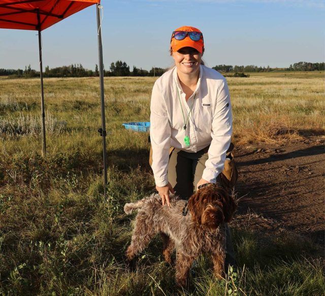 a woman smiling while bending over and holding a brown wiry haired dog