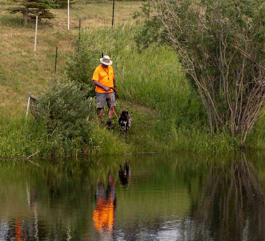 a man standing next to a lake with a dog