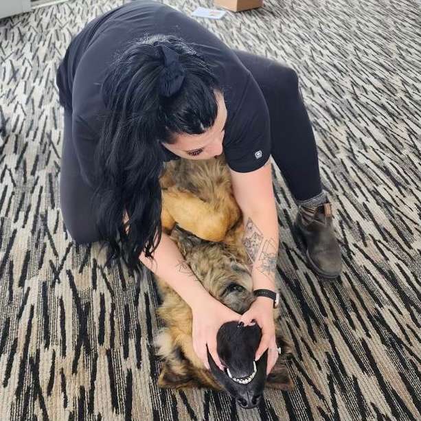 a woman kneeling down over a dog with her hands around its snout